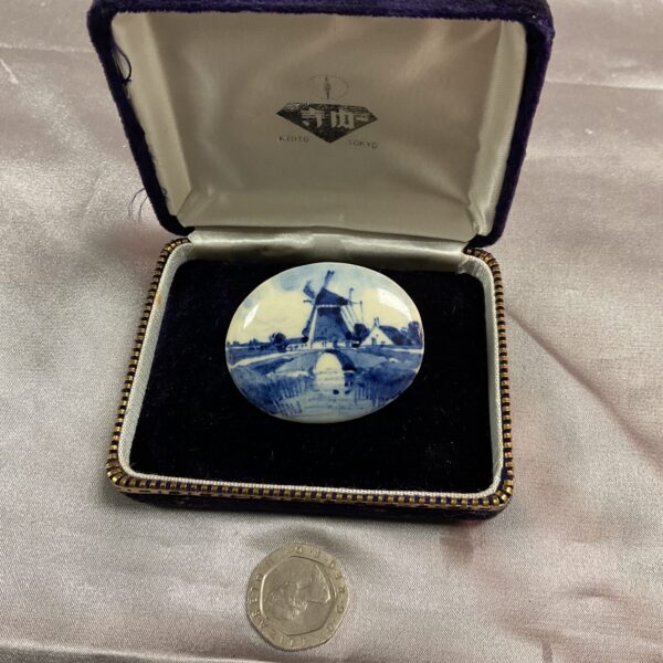 Antique delft brooch with a windmill scene in blue and white.