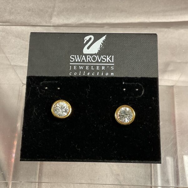 Close-up of sparkling Swarovski crystal stud earrings in gold tone.