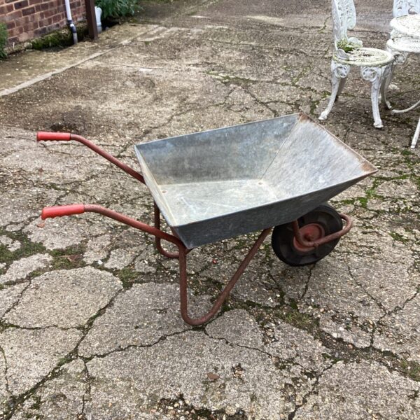Vintage galvanised wheelbarrow with red handles in a garden setting.