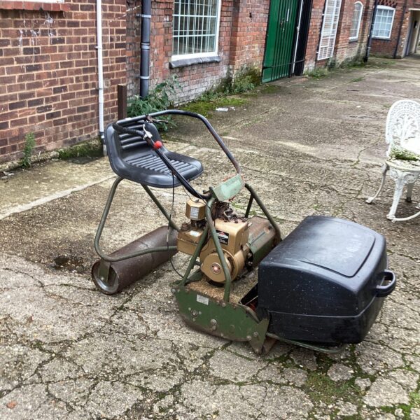 Vintage ride on cylinder mower in a garden setting.