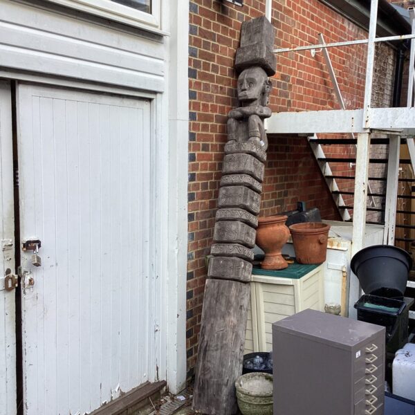 Front view of a weathered hand-carved totem pole in a garden setting.