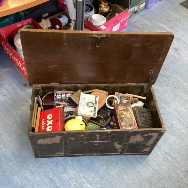 Open vintage oak chest with mixed contents on a grey floor.