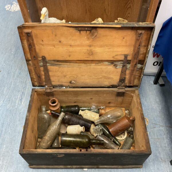 Open antique wooden trunk filled with vintage bottles.