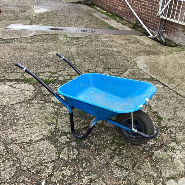 Front view of a metal builders wheelbarrow in a garden setting.