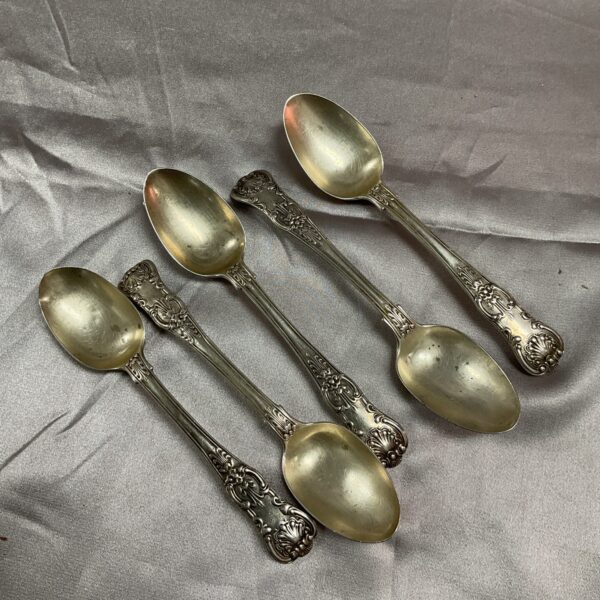 Group of five antique Georgian silver teaspoons with ornate handles.