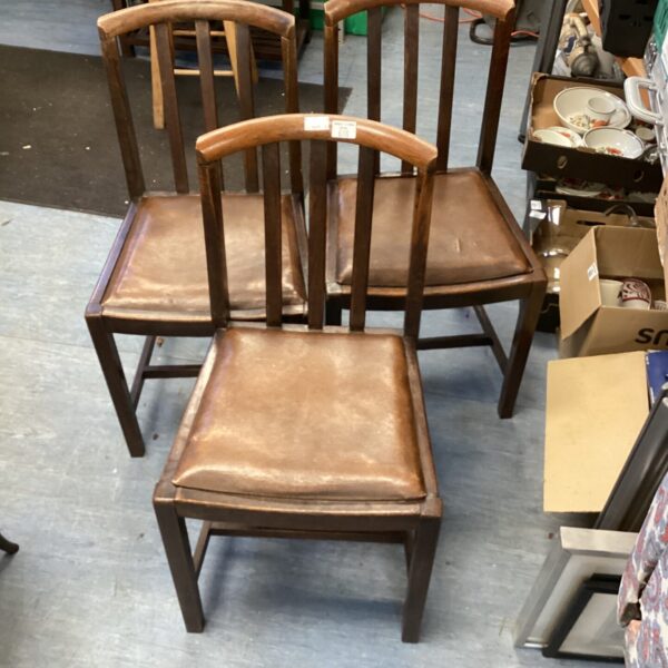 Three vintage leather dining chairs with wooden frames.