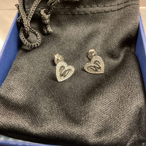 Close-up of silver heart stud earrings on a dark background.