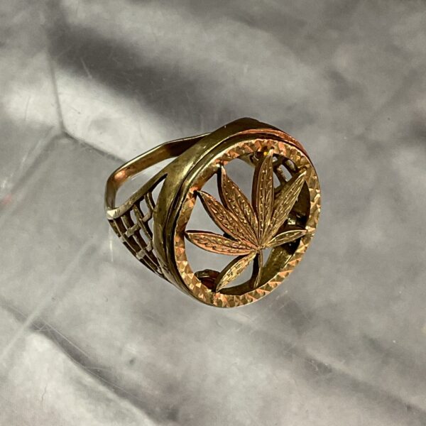 Close-up of 9ct gold cannabis leaf ring on a textured surface.