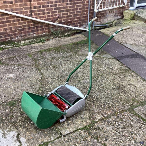 Vintage Ransmes 12” Ajax push lawn mower in a garden setting.