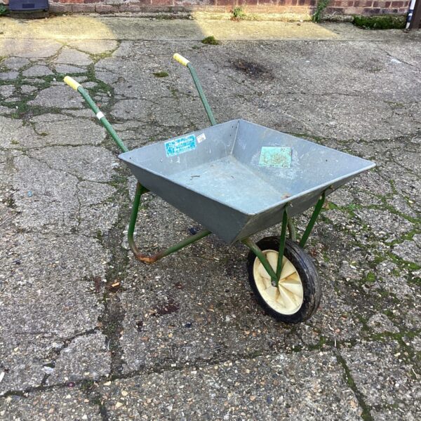 Rusty metal wheelbarrow with a single rubber wheel in a garden setting.