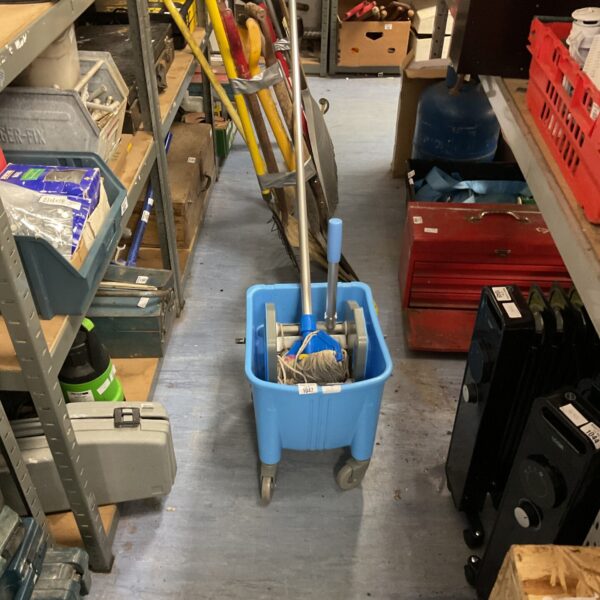 Blue cleaning bucket with mop in a storage area.