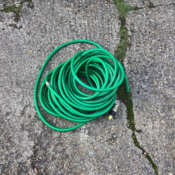 Green rubber garden hose pipe laid on a textured surface.