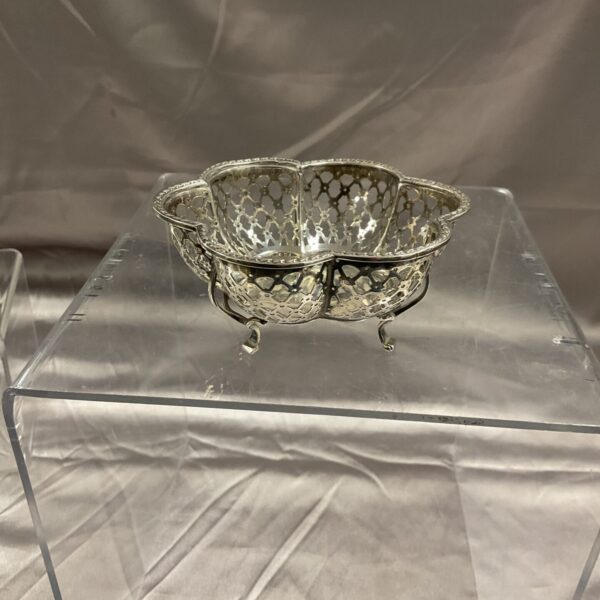 Silver bonbon dish with pierced design on a clear stand.
