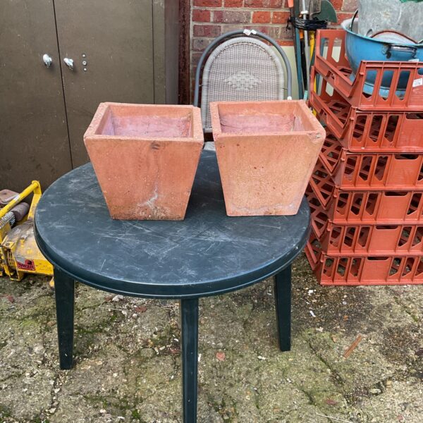 Two weathered terracotta garden planters in a garden setting.