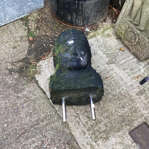 Weathered stone garden head ornament in a garden setting.