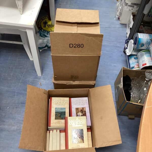 Stack of vintage Catherine Cookson novels in a cardboard box.
