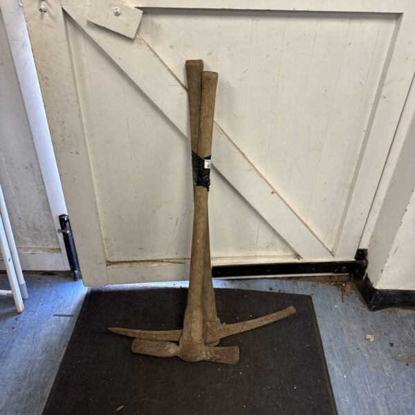 Antique mattock and pickaxe leaning against a wall.