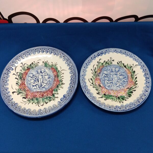 Vintage majolica wall plates with floral and cherub designs.