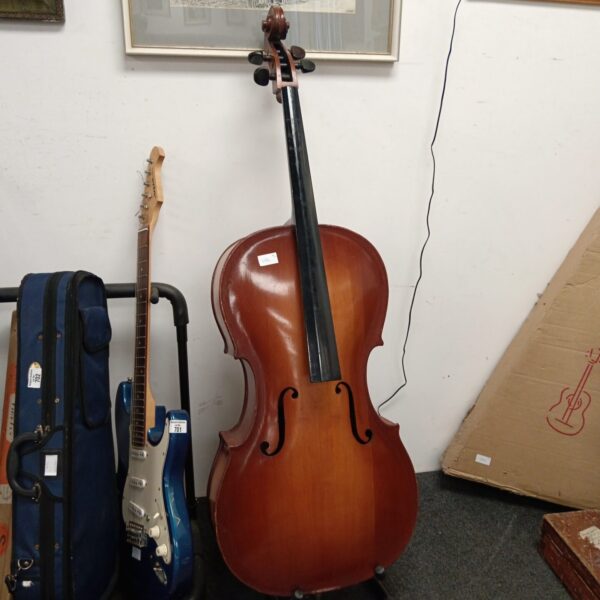 Vintage cello with a guitar in the background, awaiting restoration.