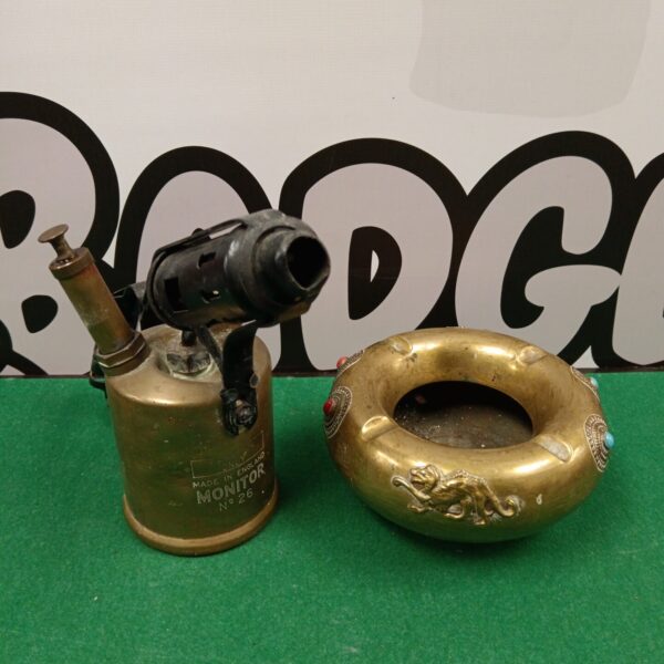 Vintage brass Monitor blow torch and Indian ashtray on display.
