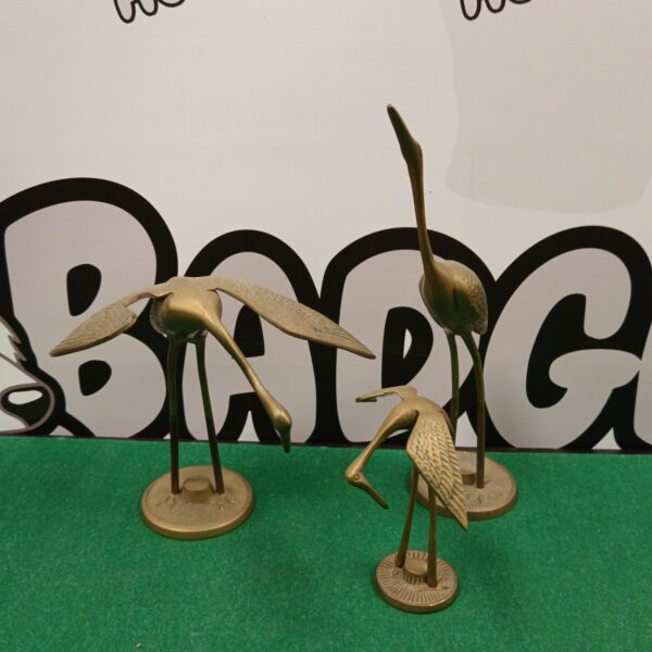 Vintage brass crane bird ornaments displayed on a green surface.
