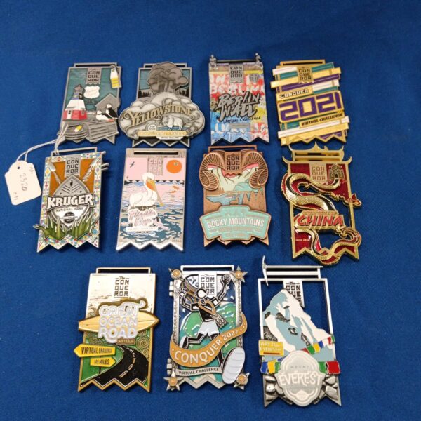 Collection of colourful Conqueror Challenge medals and enamel pins.