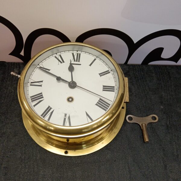 Vintage brass ships clock with white enamel dial and Roman numerals.