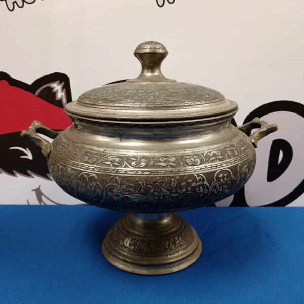 Intricate silver plate lidded pot on a dark background.