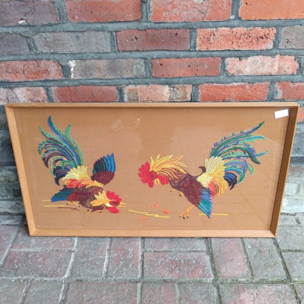 Vintage embroidery of two vividly coloured fighting cocks.