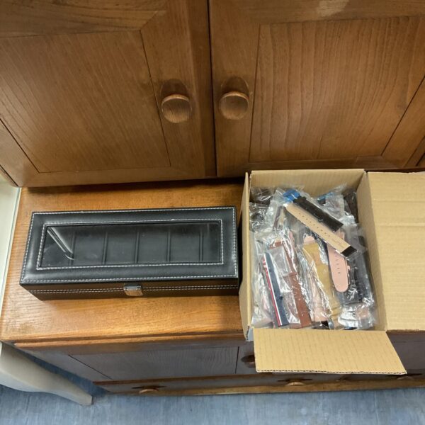 Wooden watch storage box with new watch straps inside packaging.