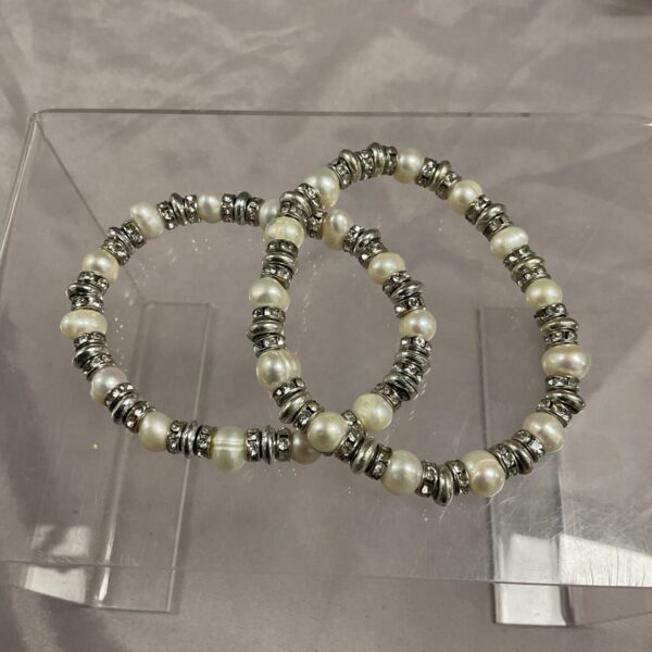 Pair of pearl and silver bracelets on a neutral background.