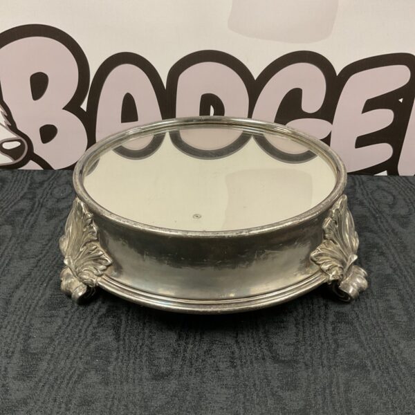 Antique silver plate cake stand with mirrored surface and ornate detailing.