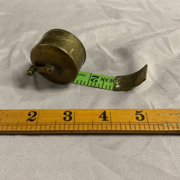 Vintage brass reel tape measure with retractable steel tape.