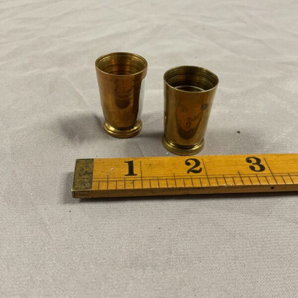 Pair of vintage brass shot cups on a white surface.