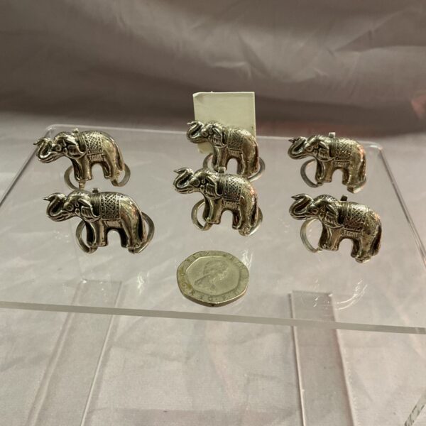 Set of six silver elephant place card holders on a white surface.