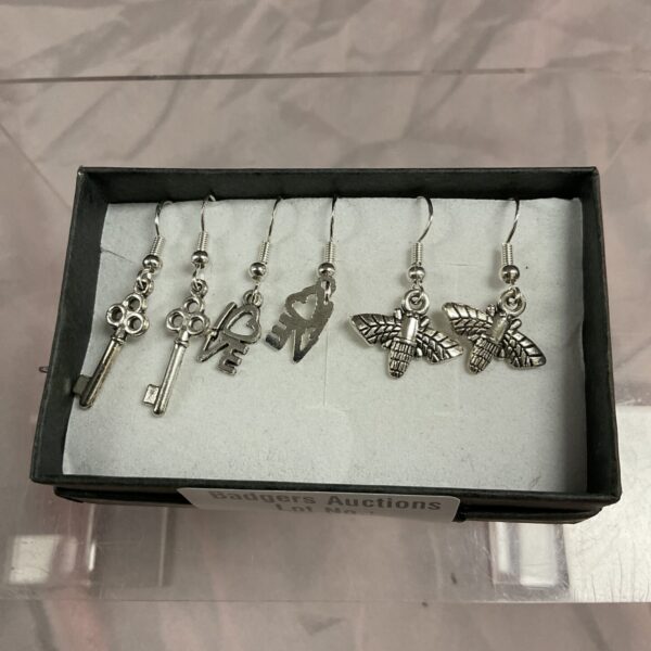 Close-up of 925 silver earrings with floral, insect, and key designs.