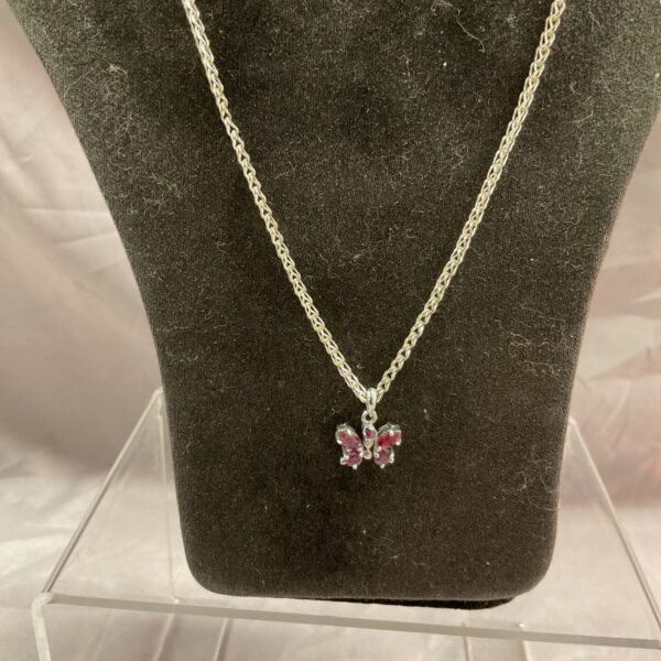 Close-up of a silver chain necklace with a red garnet butterfly pendant.