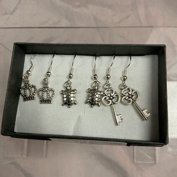 Close-up of three pairs of 925 silver earrings with floral, crown, and key designs.