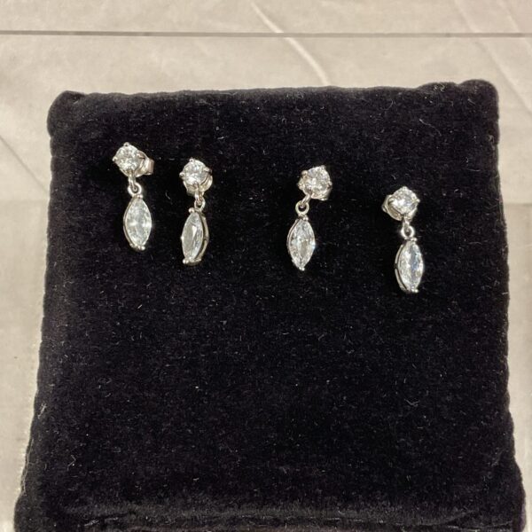 Close-up of two pairs of silver stud earrings with white stones.