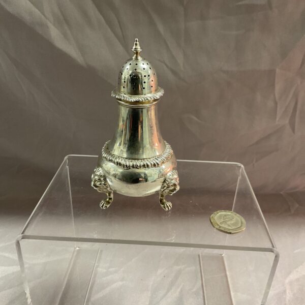 Antique sterling silver sugar sifter on a clear stand.