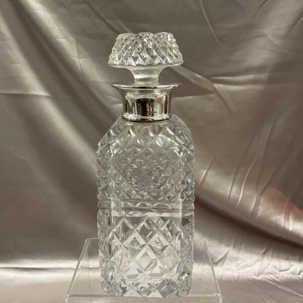 Antique silver collared crystal decanter on a display stand.