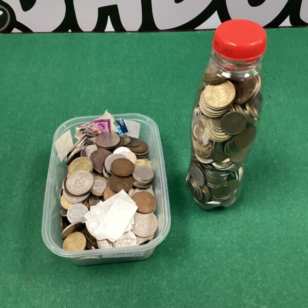 Assorted foreign coins in a plastic tub and glass bottle.