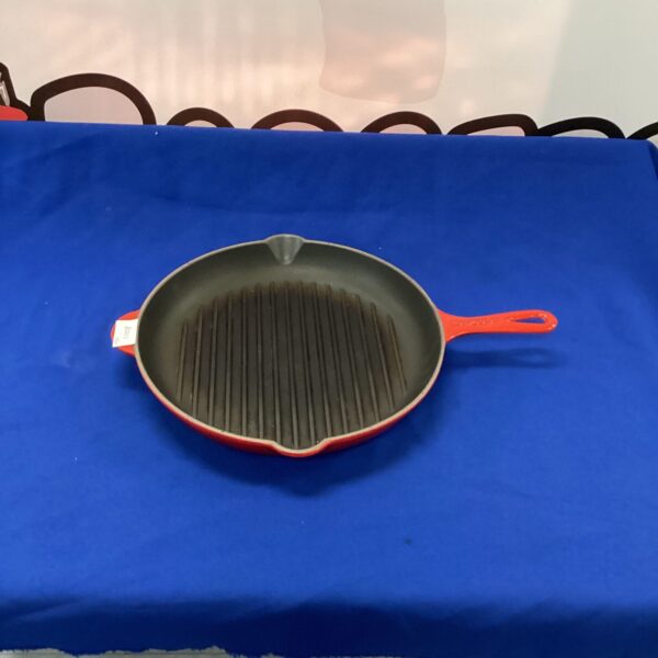 Red Le Creuset griddle pan on a white surface.