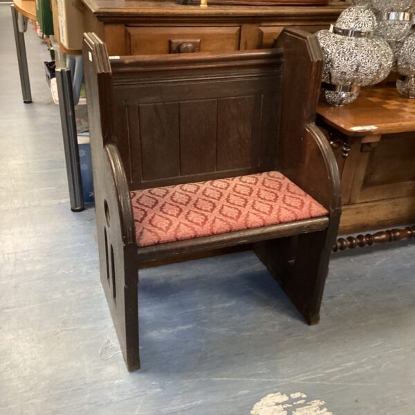 Antique oak church pew with patterned cushion, vintage religious furniture.