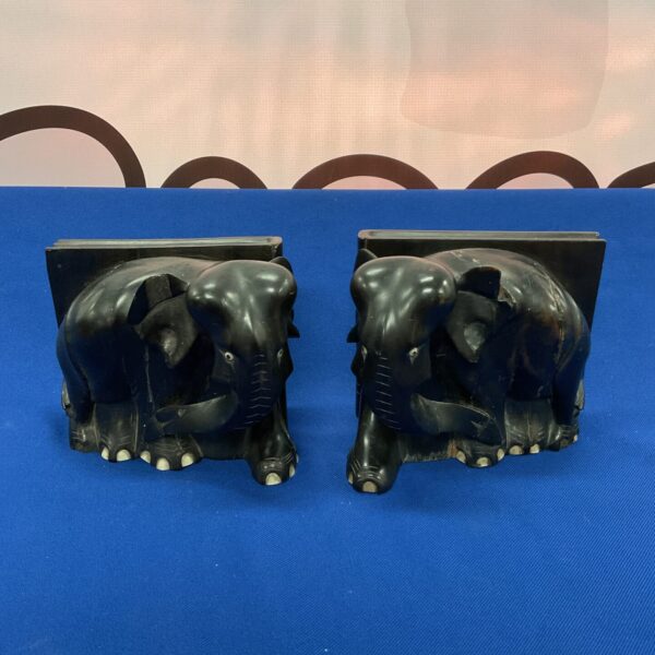 Vintage ebony elephant bookends on a dark surface.