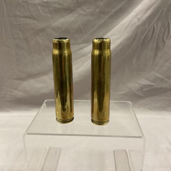 Two 1942 20mm brass shell casings displayed on a clear stand.