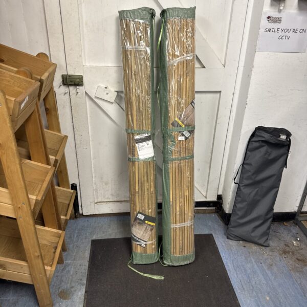 Two rolled bamboo slat fences leaning against a wall.