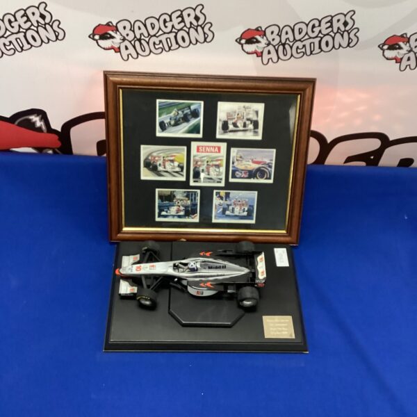 Framed display of Ayrton Senna racing memorabilia and a scale model car.
