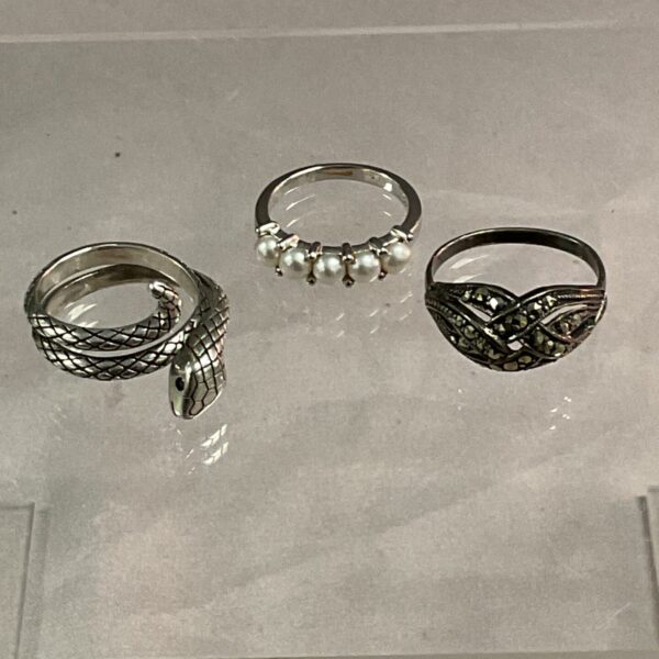 Close-up of three silver rings, including pearl and crystal designs.