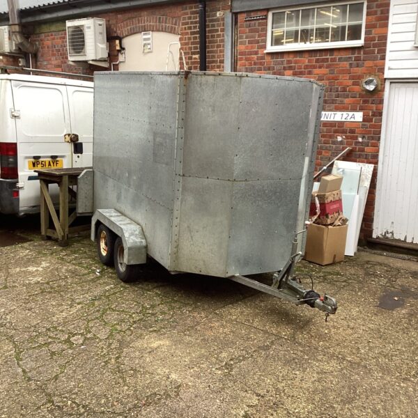 Silver aluminium trailer with twin axles parked on gravel.